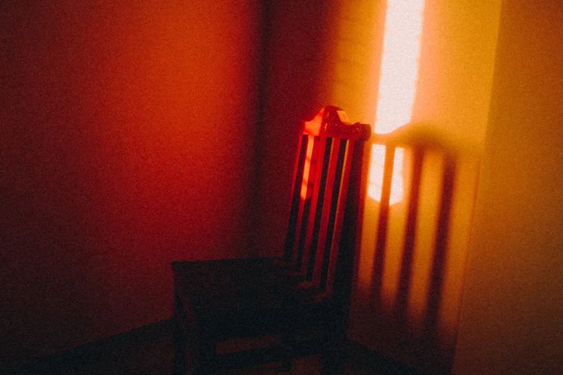 A glowing orange chair bathed in soft, mysterious light, set against a dark, shadowy backdrop.