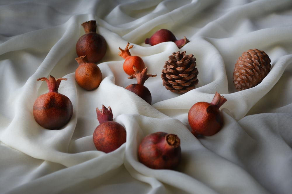 a bunch of pomegranates and a pine cone on a white cloth