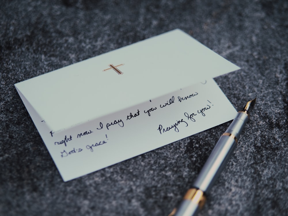 a note with a cross on it next to a pen