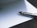 A close-up of a fountain pen with a silver and black nib resting on a blank sheet of paper. The pen's metallic components have a polished finish, reflecting light subtly. The scene is captured on a smooth, soft-focus background, creating a calm and gentle atmosphere.