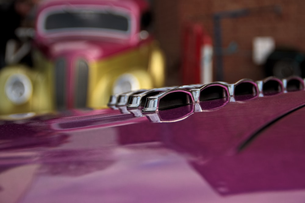 a close up of a pink car with a yellow truck in the background