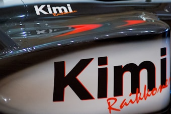 A close-up view of a vehicle part with the name 'Kimi Raikkonen' prominently displayed. The surface is sleek and shiny, with reflections indicating a polished finish. The text is printed in bold black letters with a red underline.