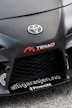 The image features the front part of a car with a focus on the bumper and grill area. Prominently displayed is the Toyota logo in the center of the car's hood. Nearby, there are several decals, including the words 'TENACI Parts for Racecars' in white with a red gear graphic, and 'altigarasjen.no' along with the 'Pandem' logo.