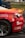 A close-up of a damaged sports car with a vibrant red and orange rear section. The car features several logos and text, including 'VVS Fagmann' and 'Bergen Gokart'. The vehicle has a visible dent and scratches near the wheel, indicating it has been involved in some rough activity. The wheel is gray with a five-spoke design. The scene is likely at a racing event, suggested by the setting and condition of the car.