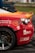 A close-up of a damaged sports car with a vibrant red and orange rear section. The car features several logos and text, including 'VVS Fagmann' and 'Bergen Gokart'. The vehicle has a visible dent and scratches near the wheel, indicating it has been involved in some rough activity. The wheel is gray with a five-spoke design. The scene is likely at a racing event, suggested by the setting and condition of the car.