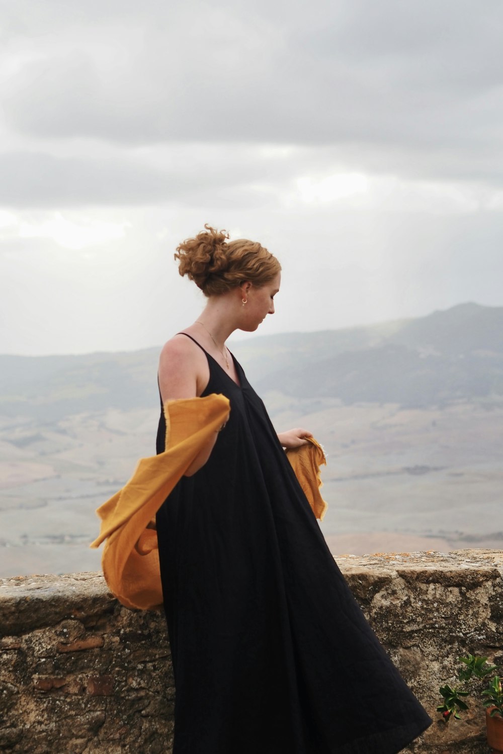 a woman in a black dress standing on a stone wall