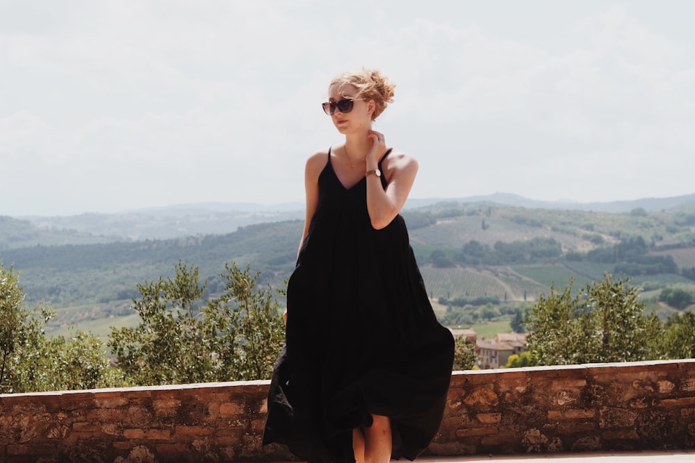 a woman in a black dress standing on a stone wall