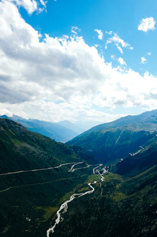 A winding river cutting through the lush green valleys of Kaghan under a bright blue sky.