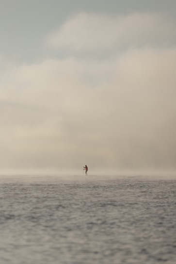 A serene lake at dawn with a person paddleboarding calmly, surrounded by soft mist and gentle light.