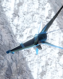 A futuristic, sleek aircraft with a blue and silver design is flying over a snowy mountainous terrain. The structure of the aircraft resembles a combination of a plane and a drone with fins and rotors. The snow on the ground contrasts with the sky and adds a dynamic visual element.