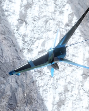A futuristic, sleek aircraft with a blue and silver design is flying over a snowy mountainous terrain. The structure of the aircraft resembles a combination of a plane and a drone with fins and rotors. The snow on the ground contrasts with the sky and adds a dynamic visual element.