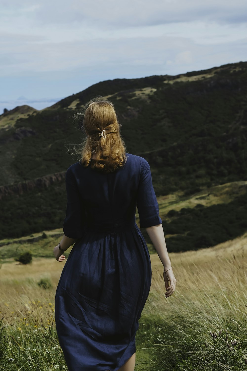 eine Frau in einem blauen Kleid, die durch ein Feld geht