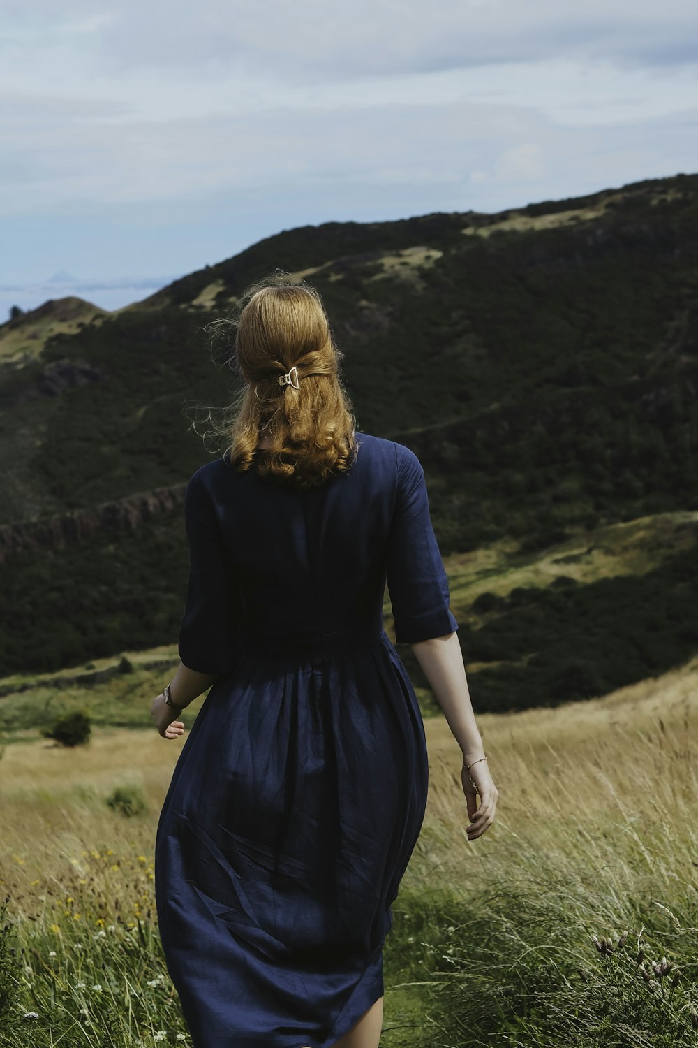 a woman in a blue dress walking through a field