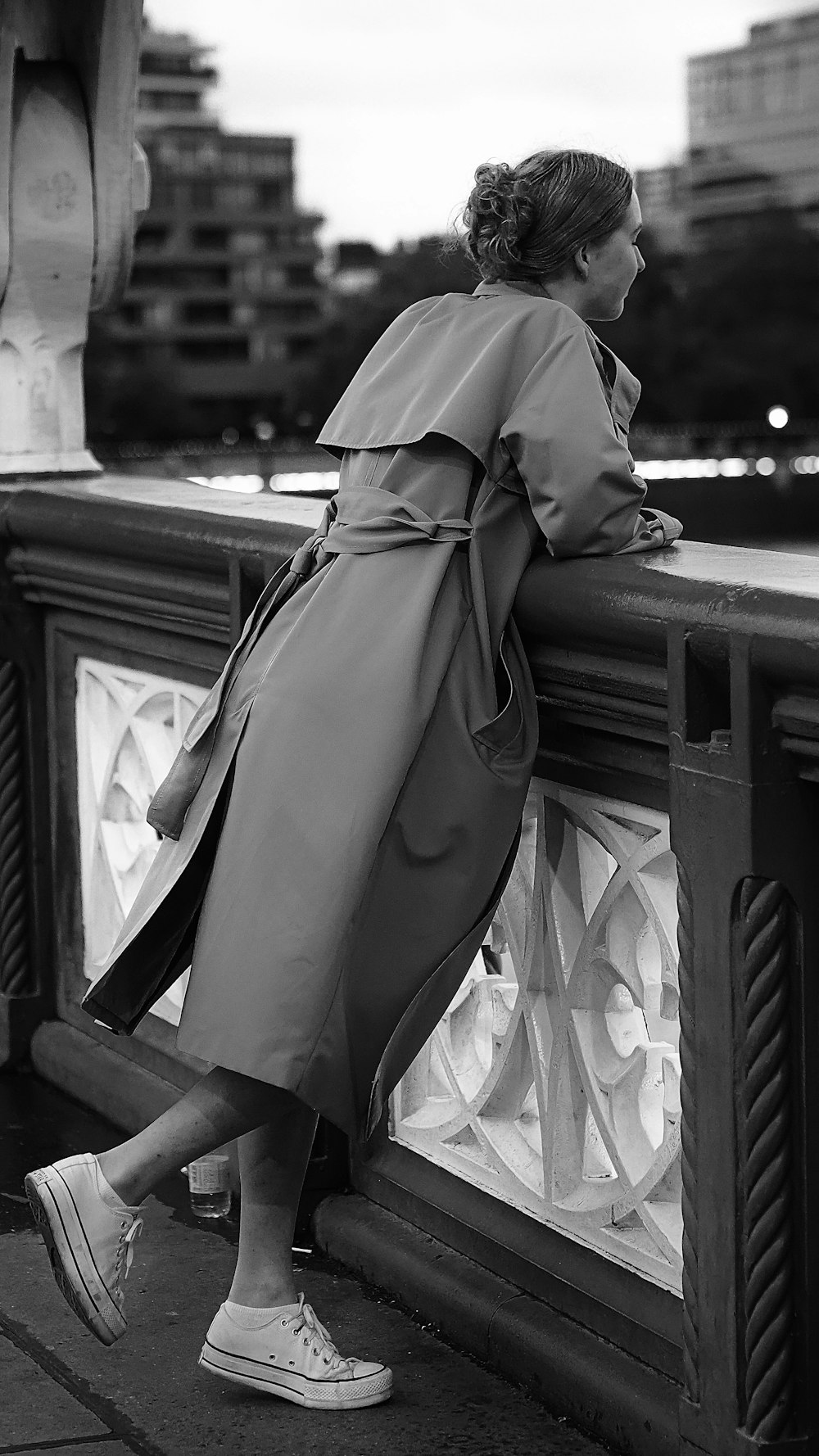 a woman in a trench coat leaning on a railing