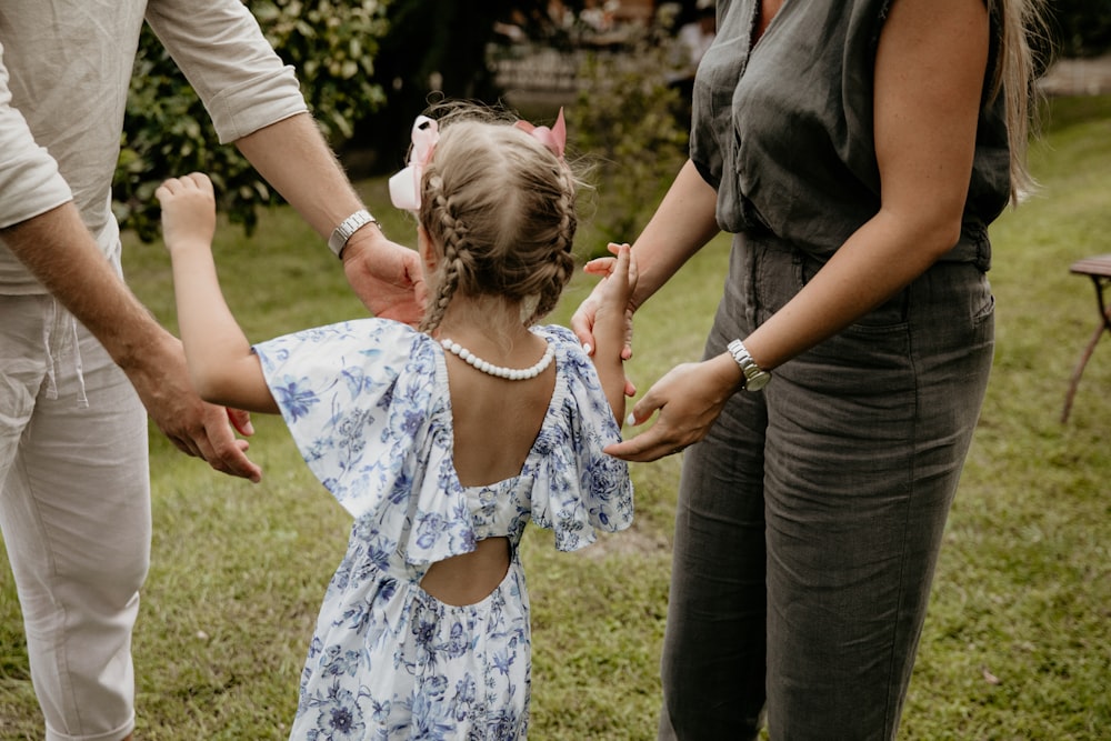 a little girl in a blue dress holding hands with her parents
