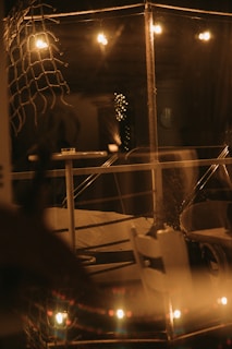 Warm lighting creates a cozy atmosphere in a dimly lit space featuring a table and chairs. Rope decorations add a nautical flair, while strings of lights provide a soft glow, enhancing the tranquil and intimate setting.