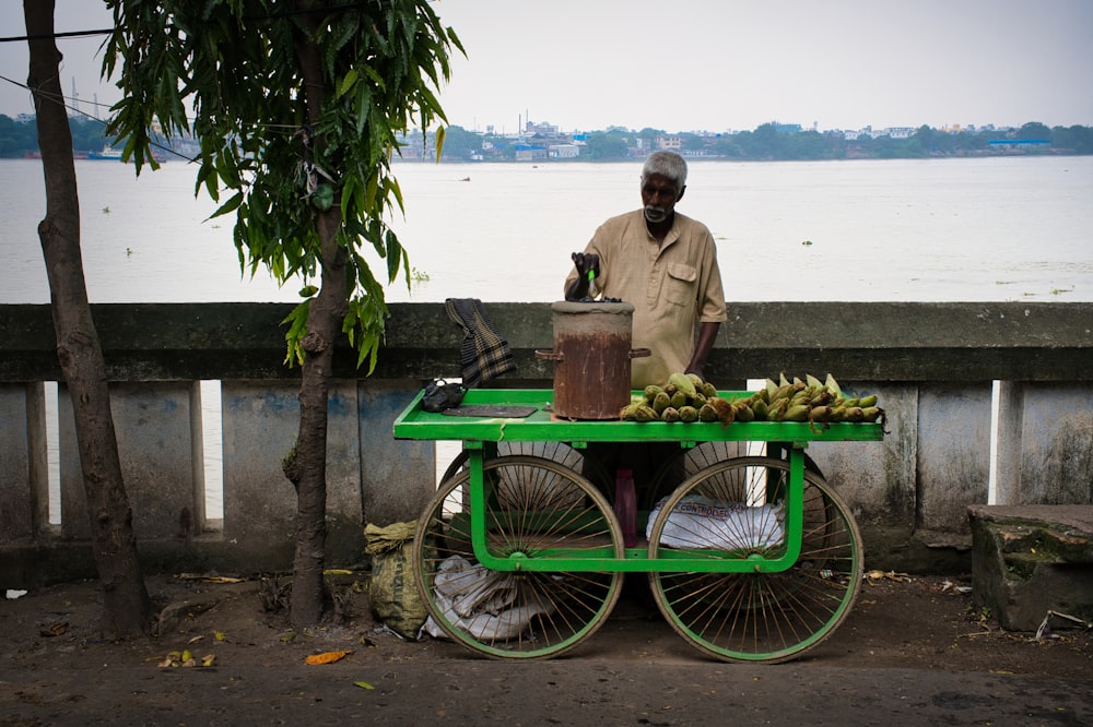 a man standing next to a green cart filled with bananas