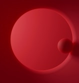 A minimalist design featuring two red spheres, one larger and one smaller, against a red backdrop. The image emphasizes smooth gradients and shadows, creating a sense of depth.