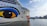 The image features a large cruise ship with a distinctive eye and lip design painted on its hull. The ship is named AIDAnova and is docked at a port. In the background, there are calm waters and a mountainous landscape under a partly cloudy sky.