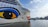 The image features a large cruise ship with a distinctive eye and lip design painted on its hull. The ship is named AIDAnova and is docked at a port. In the background, there are calm waters and a mountainous landscape under a partly cloudy sky.