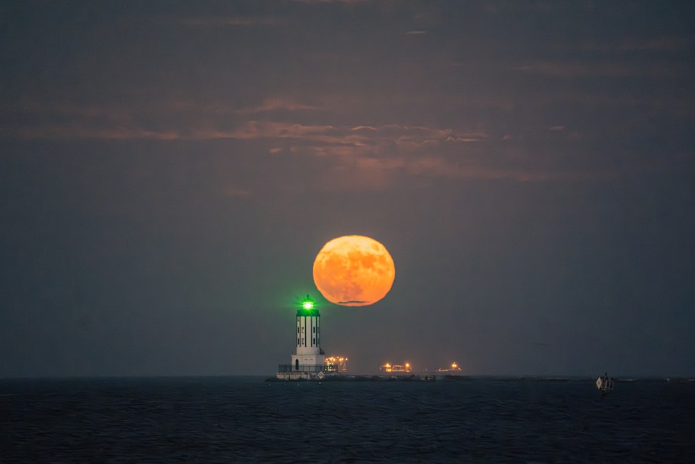 a full moon rising over a lighthouse in the ocean