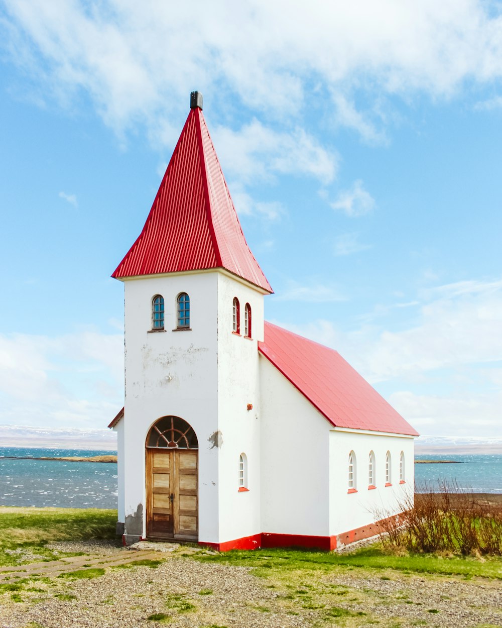 a white church with a red roof next to a body of water