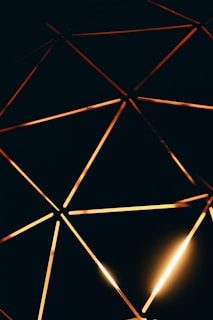 Geometric lines intersect in a pattern of interconnected triangles and other shapes, illuminated with a warm golden light against a dark background.