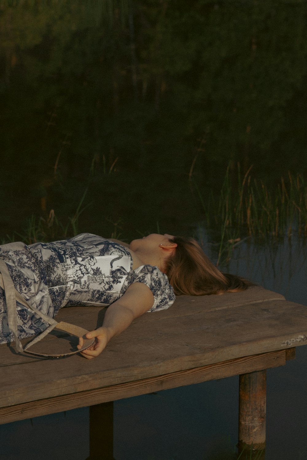 a woman laying on a wooden dock next to a body of water