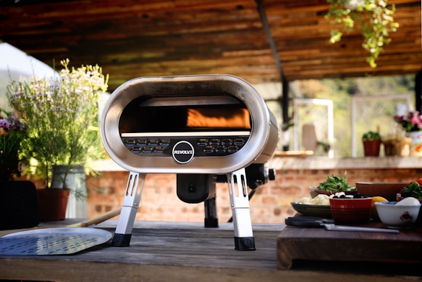 A sleek double-fuel pizza oven combining gas and wood, showcasing its stainless steel finish.