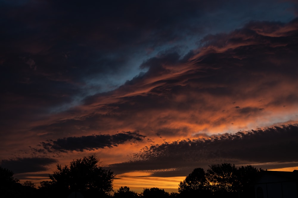 a sunset with clouds and trees in the foreground