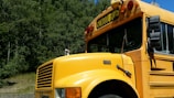 A bright green mini school bus parked outside a sunny elementary school with happy children boarding.