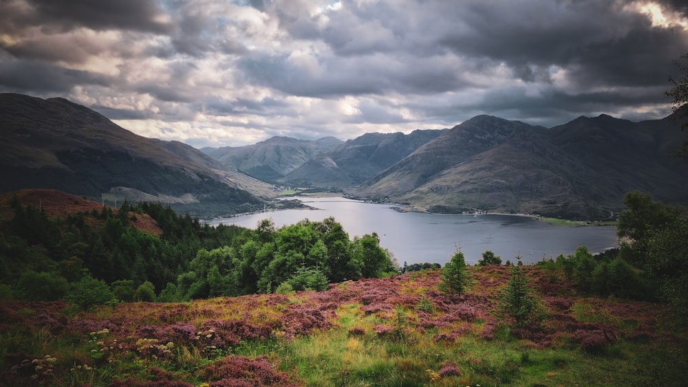 a lake surrounded by mountains under a cloudy sky