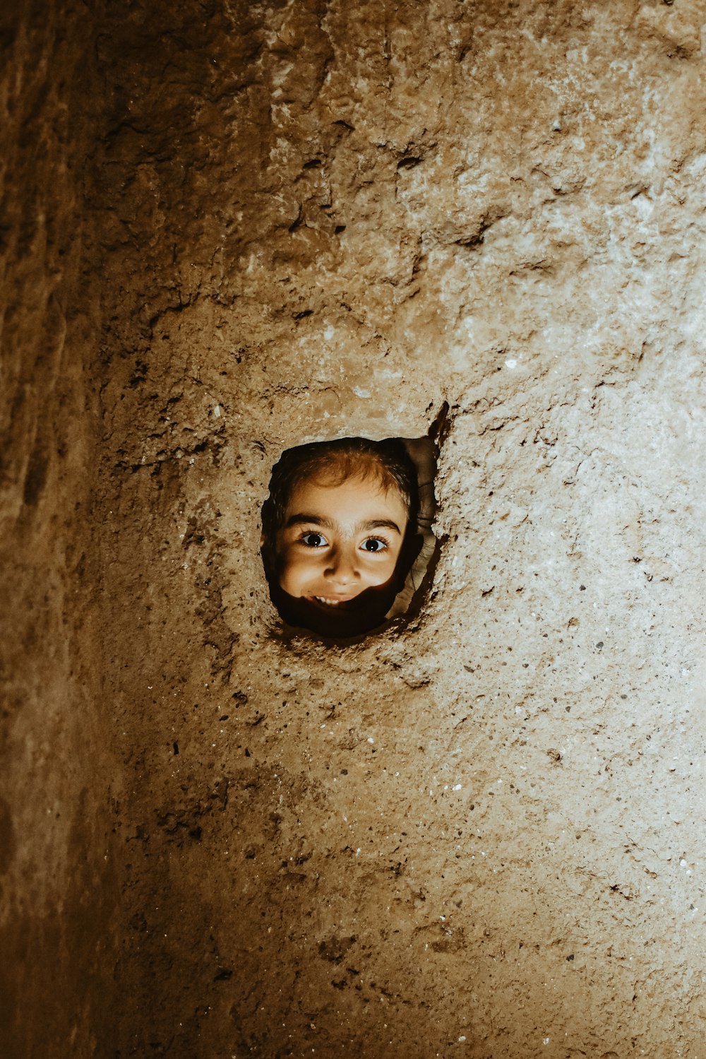 a small child peeking out of a hole in a wall