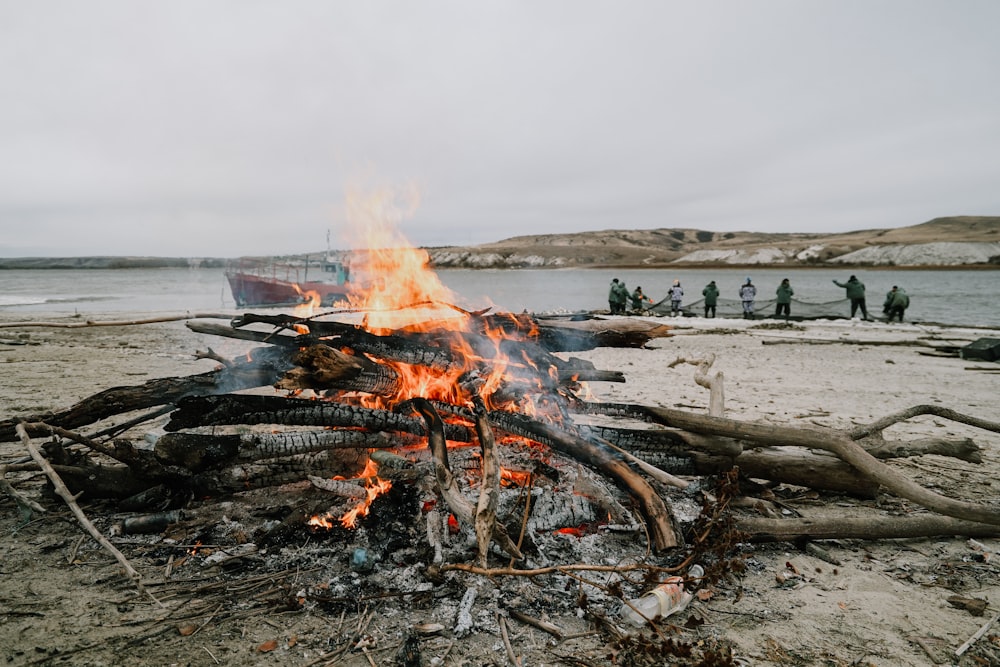 a campfire on a beach with a boat in the background