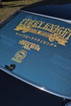 A rear windshield of a car features decorative gold lettering and symbols. The text includes words like 'LUCKY KNIGHT' and 'TOUGE RUSH' with additional Japanese characters. The window is tinted, and the surface has a clean finish.
