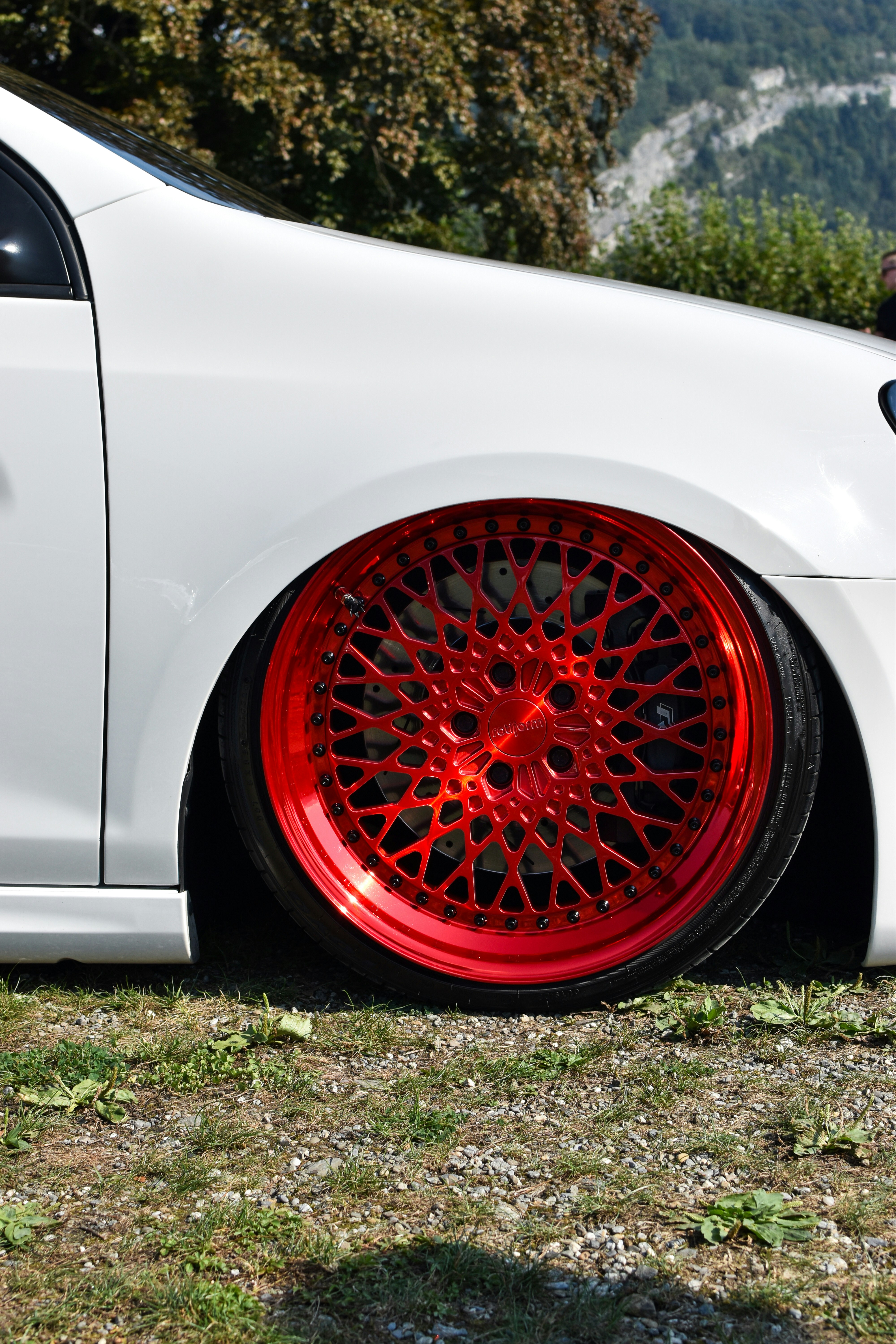 Une voiture blanche avec des jantes rouges garée dans un champ