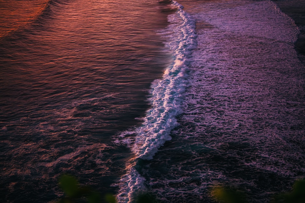 a sunset over the ocean with a wave coming in