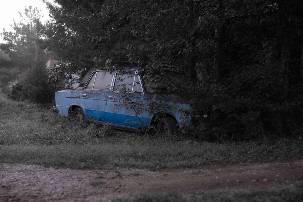 an old blue car sitting in the middle of a field