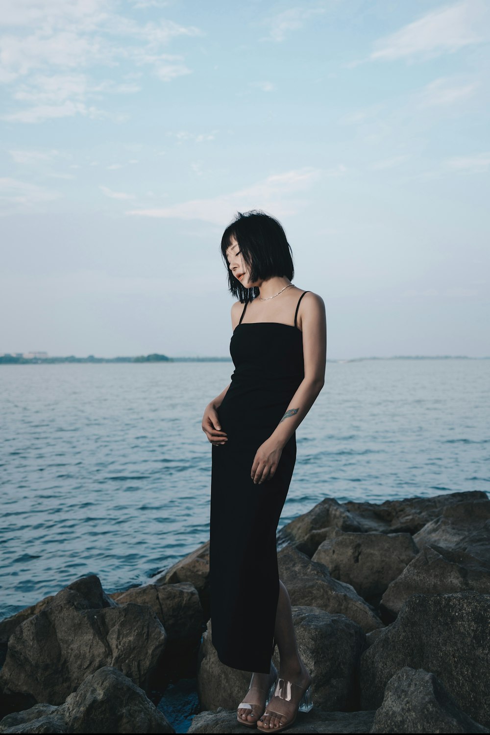 a woman in a black dress standing on rocks by the water