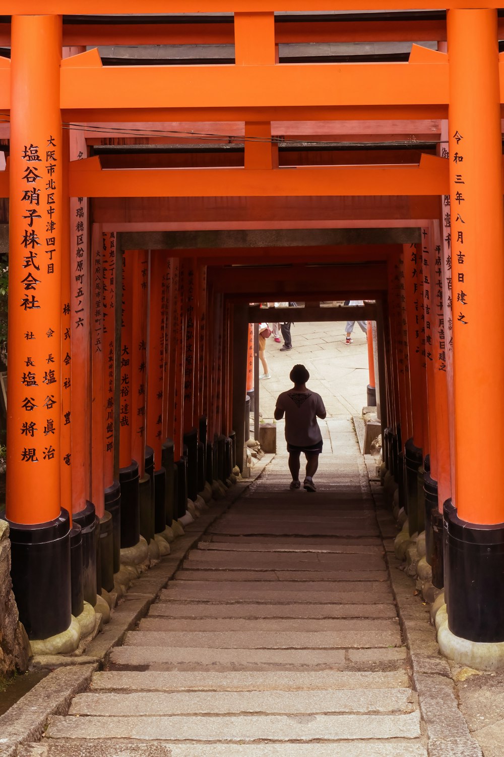 a man walking down a walkway under an orange archway