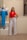 A woman stands confidently beside a mannequin dressed in a blue two-piece outfit. She wears a red sleeveless top with white high-waisted pants and sand-colored heels. The setting appears to be an indoor boutique or fashion store with neutral-colored walls and wood flooring.