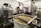 A brewery setup with stainless steel tanks labeled 'Mash' and 'Boil', surrounded by other large tanks and industrial equipment. A bag filled with grains is positioned in the foreground, indicating a brewing or fermentation process.