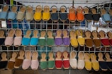 A display of various colorful sandals arranged on a metal rack at an outdoor market. Each row of the rack holds sandals of different colors including blue, yellow, orange, red, green, and more, neatly lined up.