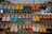 A display of various colorful sandals arranged on a metal rack at an outdoor market. Each row of the rack holds sandals of different colors including blue, yellow, orange, red, green, and more, neatly lined up.