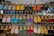 A display of various colorful sandals arranged on a metal rack at an outdoor market. Each row of the rack holds sandals of different colors including blue, yellow, orange, red, green, and more, neatly lined up.
