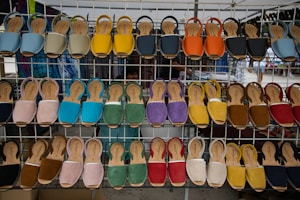 A display of various colorful sandals arranged on a metal rack at an outdoor market. Each row of the rack holds sandals of different colors including blue, yellow, orange, red, green, and more, neatly lined up.