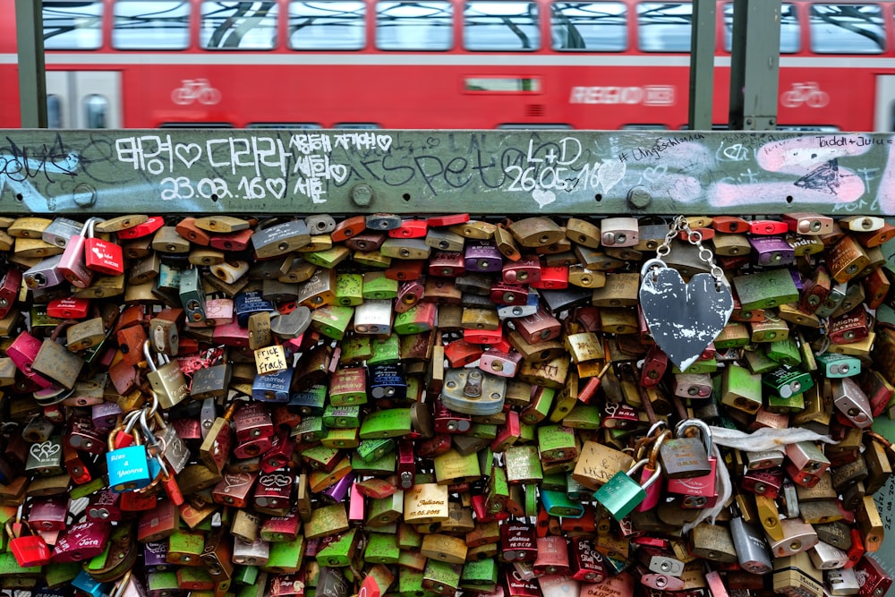 a wall covered in padlocks with a red double decker bus in the background