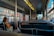Interior of a city bus with several people seated and looking out the windows. Sunlight illuminates the busy urban street outside, featuring buildings and pedestrians. The scene captures a typical public transport setting.