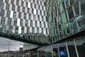 The image features a modern architectural structure with a facade composed of numerous hexagonal glass panels. Each panel reflects light and surrounding scenery, creating a complex pattern of reflections and transparency. The glass panels create an intricate, repeating geometric pattern that is both visually striking and innovative in design.