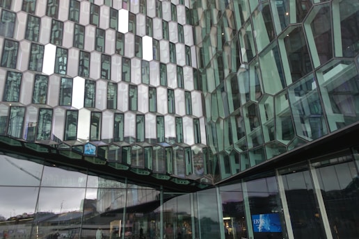 The image features a modern architectural structure with a facade composed of numerous hexagonal glass panels. Each panel reflects light and surrounding scenery, creating a complex pattern of reflections and transparency. The glass panels create an intricate, repeating geometric pattern that is both visually striking and innovative in design.
